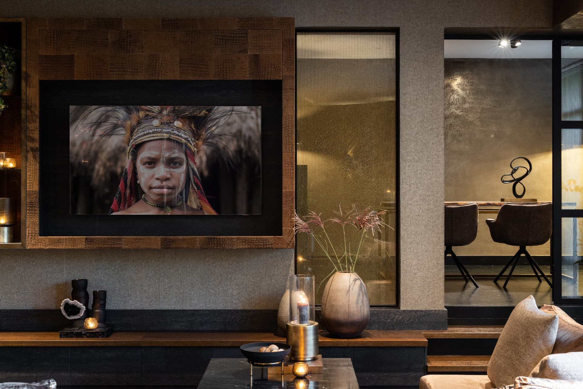 Warm, layered living space in Villa Amstelveen with tribal portrait artwork, aged timber and bronze candlelight